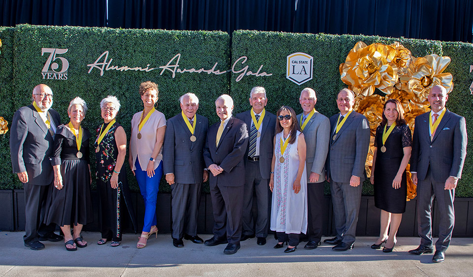 Group photo of the alumni honorees with President Covino in front of a decorative hedge celebrating the 75th anniversary and the gala.