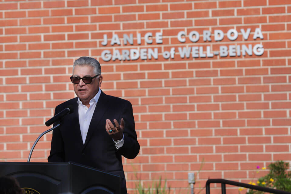 Richard Cordova speaks at lectern in front of Janice Cordova Garden of Well-Being sign.