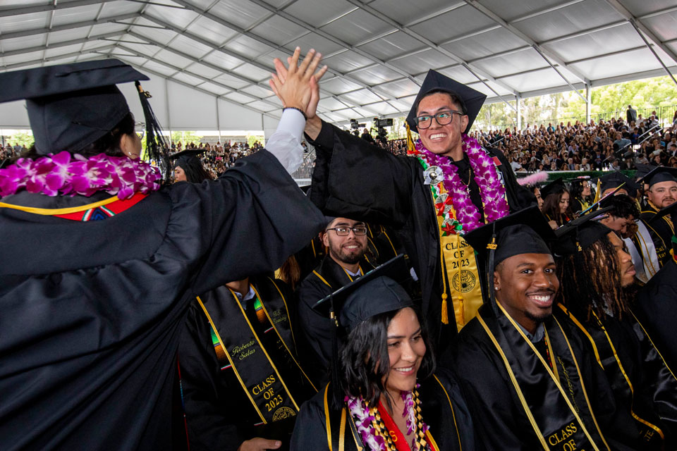 Students at a graduation ceremony give each other a high-five.