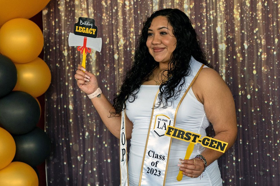 A person standing in front of a glittery background holding a small sign posing for a photo.