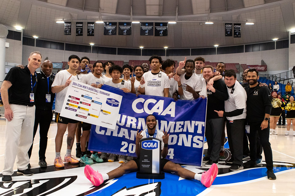 A group photo of the Cal State LA mens basketball team holding championship banners.