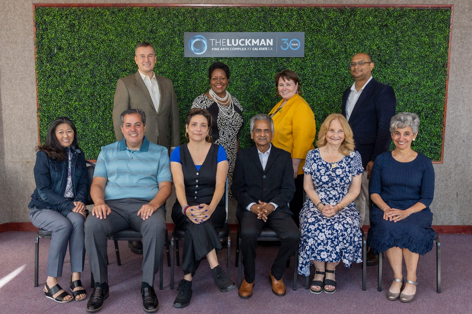 A group of professors take a photo in front of a green backdrop.