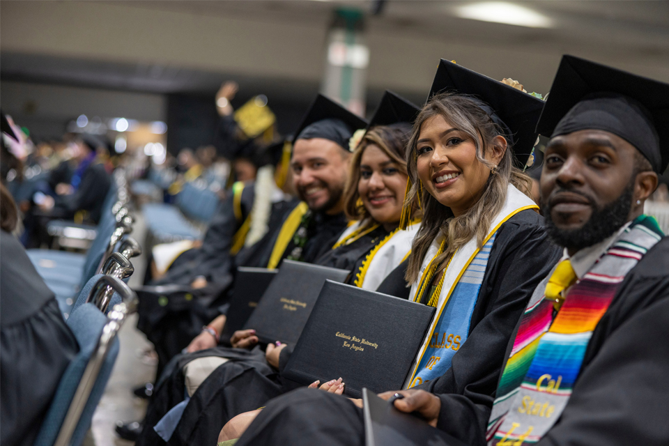 Students wearing their cap and gown sit together in a group.