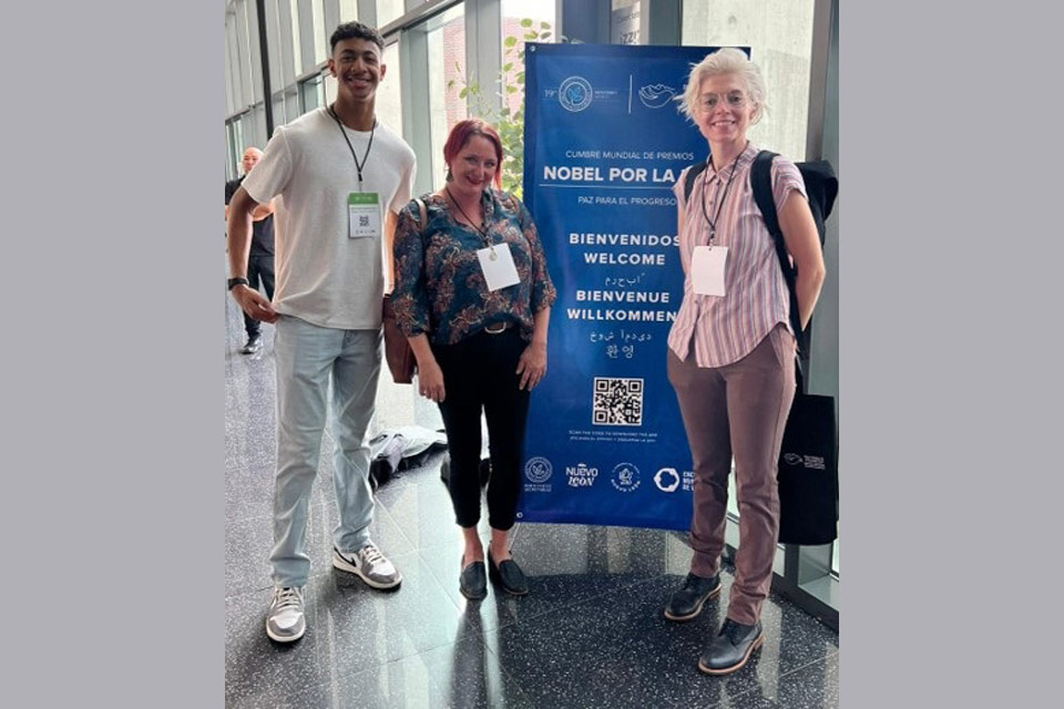 Three students stand in front of a banner welcoming participants to a conference.