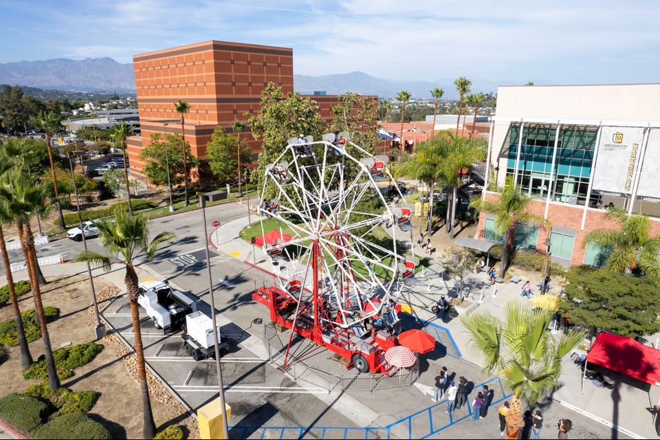 and white Ferris wheel spins in the middle of the Cal State LA campus during Campus Day, with buildings and palm trees in the background.