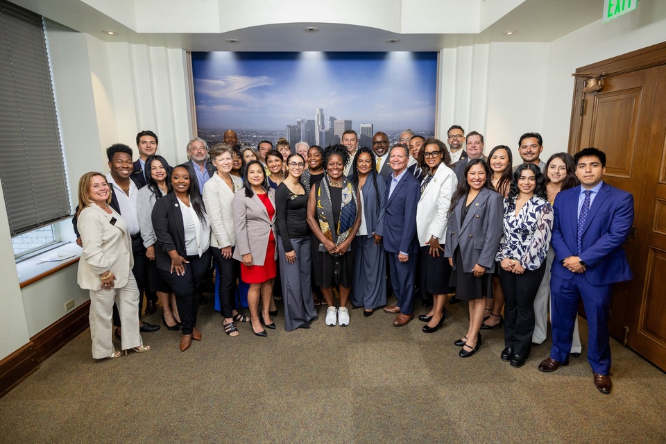 Group photo of Cal State LA leaders, staff, and city officials at Los Angeles City Hall in front of a panoramic mural of downtown LA.