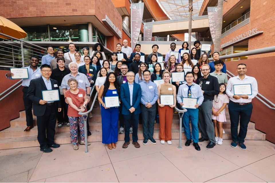 A large group of students, faculty, and staff pose on the steps outside the Cal State LA bookstore, holding certificates at a Biostart graduation event.