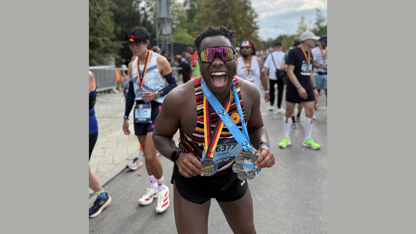 JT Chestnut celebrates after finishing the Berlin Marathon, smiling and displaying multiple medals earned through the Abbott World Marathon Majors.