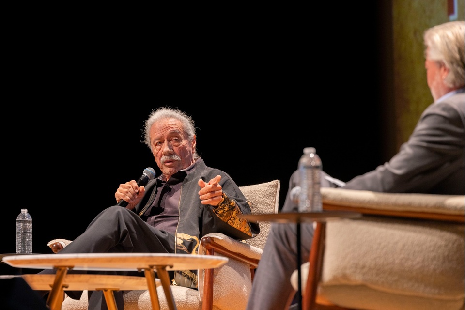 Edward James Olmos participates in an on-stage conversation during an event at Cal State LA, seated with a microphone in hand.