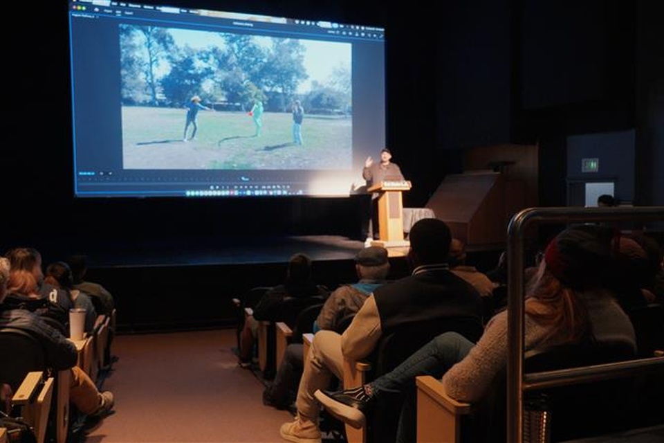 Audience seated in a theater watching a presenter at a Cal State LA podium during an AI symposium presentation.