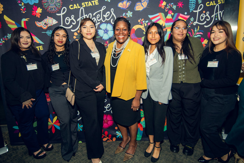 Cal State LA President stands with students in front of colorful Los Angeles backdrop at campus leadership event.