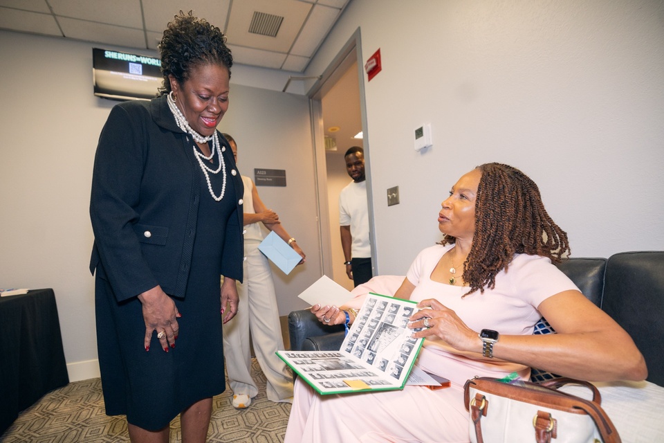 Guest greets a seated attendee reviewing a photo album inside a campus room during a Cal State LA event.