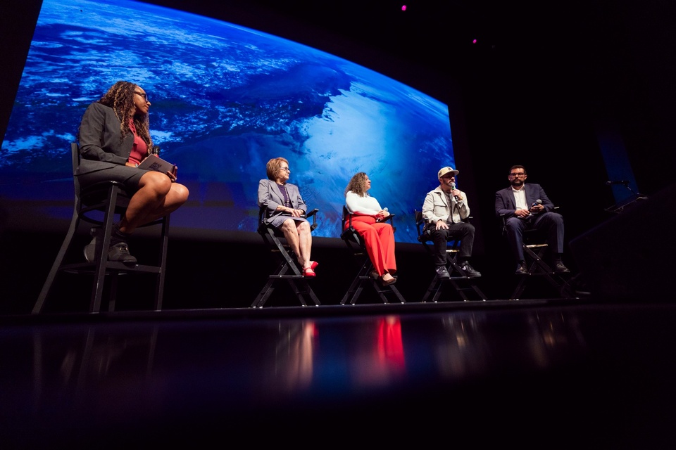 Panel of speakers sit on stage in front of a large screen displaying Earth imagery during a Cal State LA event.