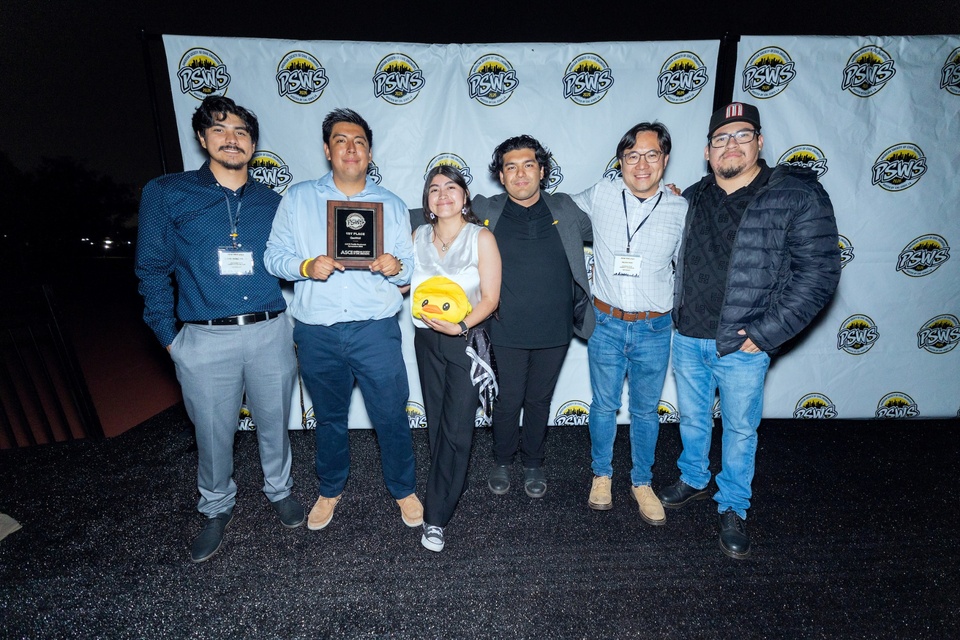Group of students stand together holding an award plaque in front of a PSWS event backdrop, posing for a photo at a recognition event.