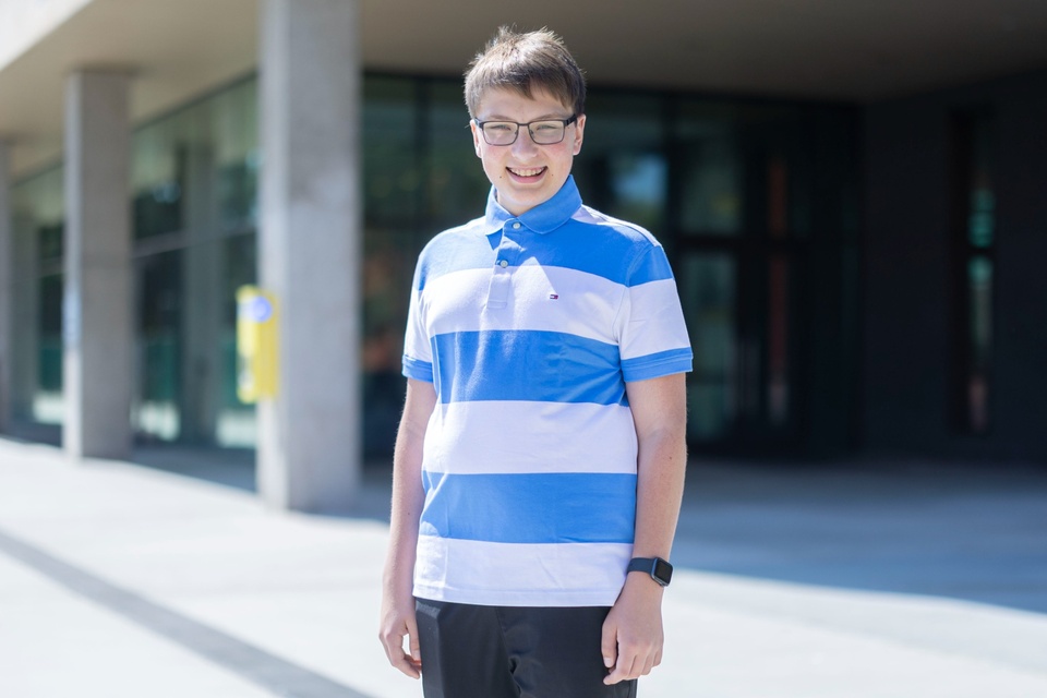 Student stands outdoors in front of a campus building, smiling in the sunlight at Cal State LA.
