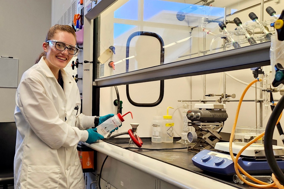 Researcher wearing a lab coat, safety glasses, and gloves works at a laboratory fume hood while handling scientific equipment at Cal State LA.