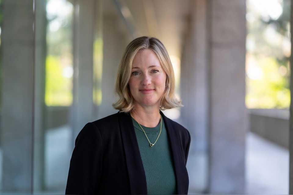 Faculty member stands in a campus corridor wearing a green top and dark blazer.