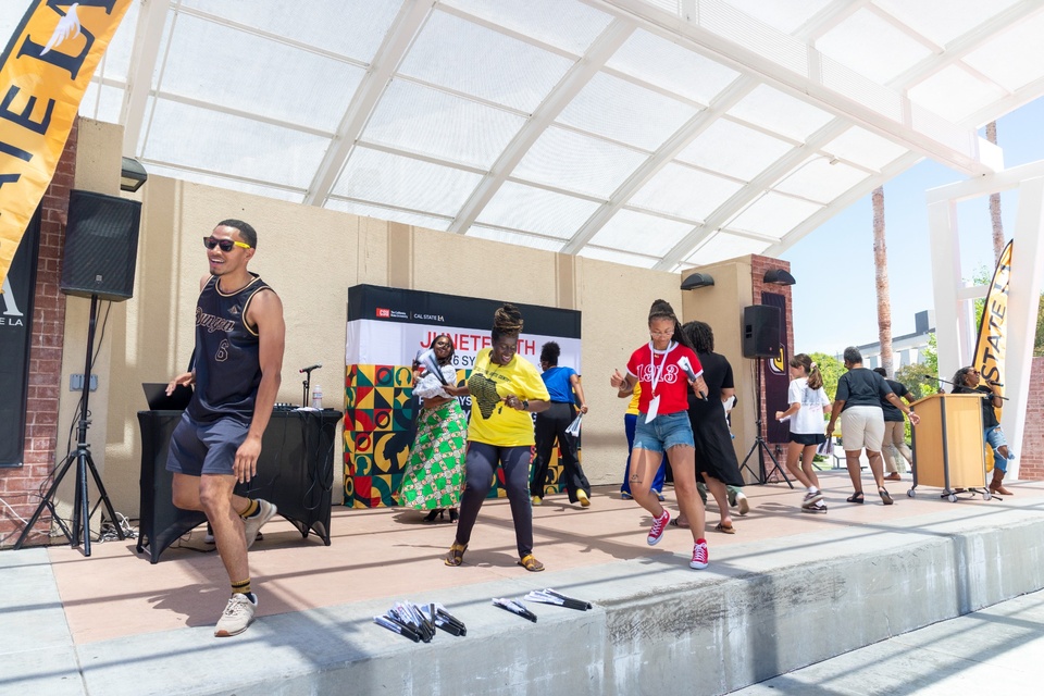 Participants dance on an outdoor stage during the Juneteenth Symposium at Cal State LA. 