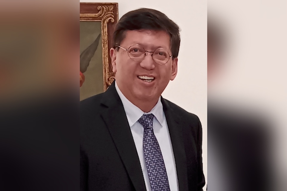 Professional portrait of an individual wearing glasses, a dark suit, and a patterned tie.