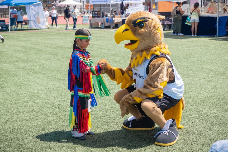 Cal State LA’s Golden Eagle mascot greets a child wearing colorful regalia during the Pow Wow.