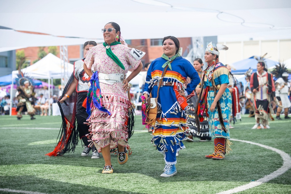 Participants wearing colorful regalia walk across the field during the grand entry at the Cal State LA Pow Wow.