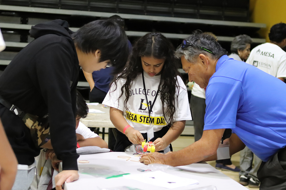 A student works on a small wheeled device with two adults during MESA STEM Day at Cal State LA.
