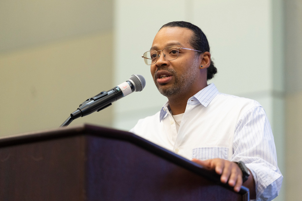 A speaker wearing glasses addresses the audience from a lectern at Cal State LA.